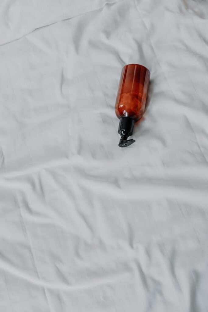 Overhead view of a brown pump bottle on a white fabric surface, minimalist product shot.