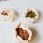 Three varieties of grains displayed in eco-friendly cloth bags on a clean surface.