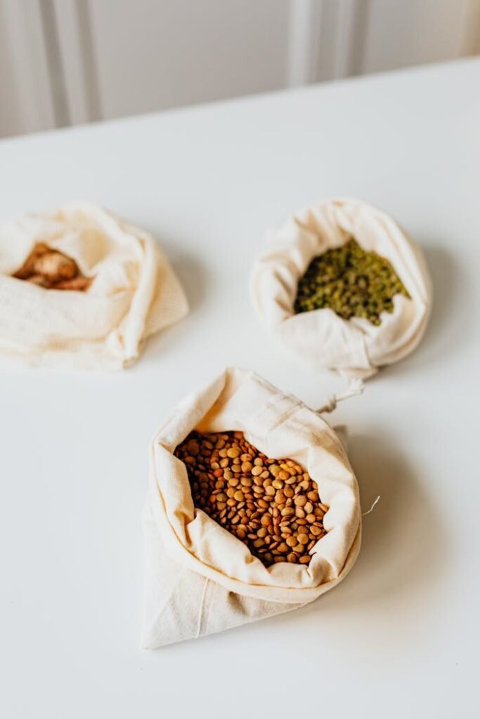 Three varieties of grains displayed in eco-friendly cloth bags on a clean surface.